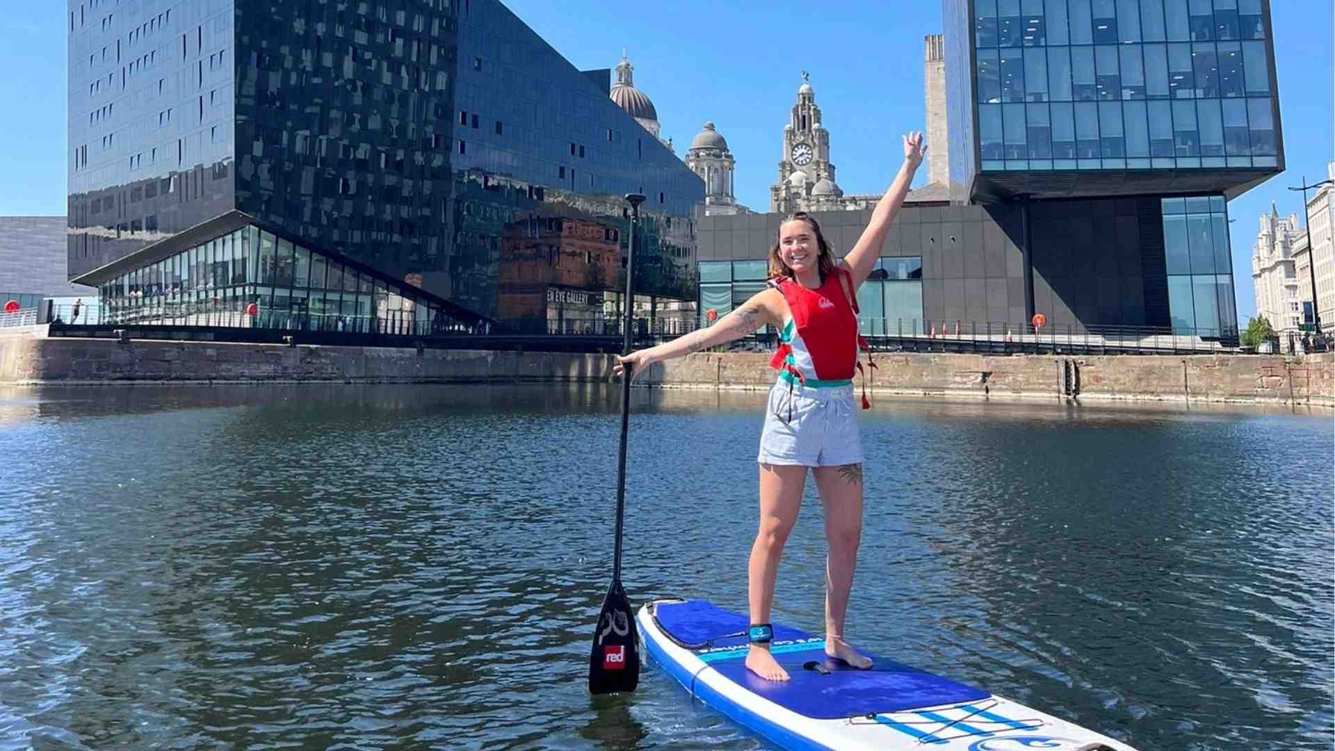 student paddleboarding on the River Mersey with the Liver Building and waterfront behind her