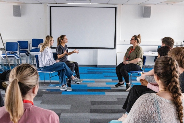 Two students engage in a role play activity with the Deaf facilitator, practicing communication techniques in a small circle.
