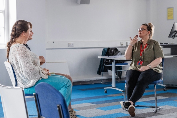 A student doctor sits across from the Deaf facilitator in a one-on-one setting, practicing sign language and expressive communication.
