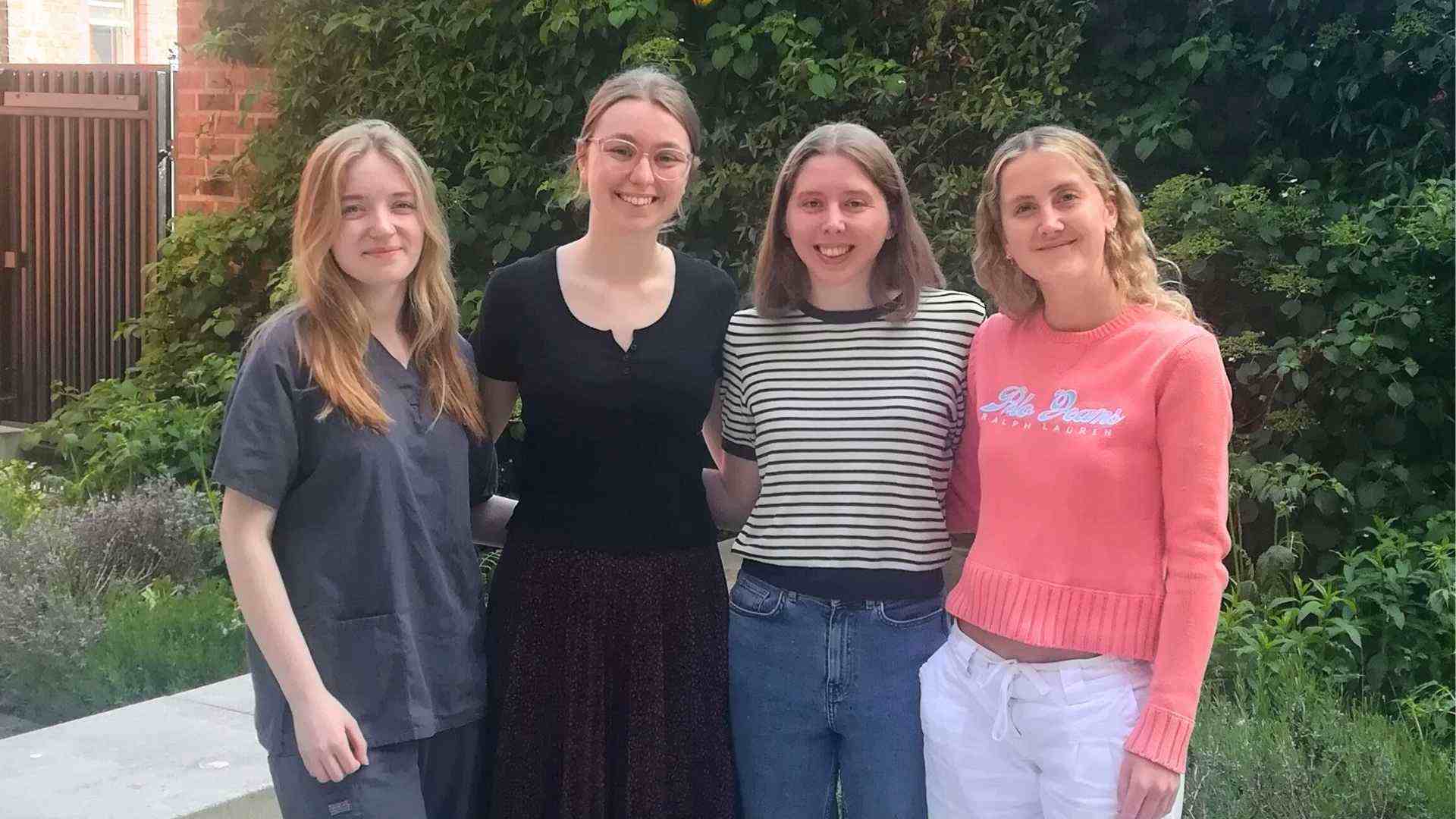 Four student doctors from the Liverpool Oncology Society standing together outdoors, smiling in front of a leafy green background.