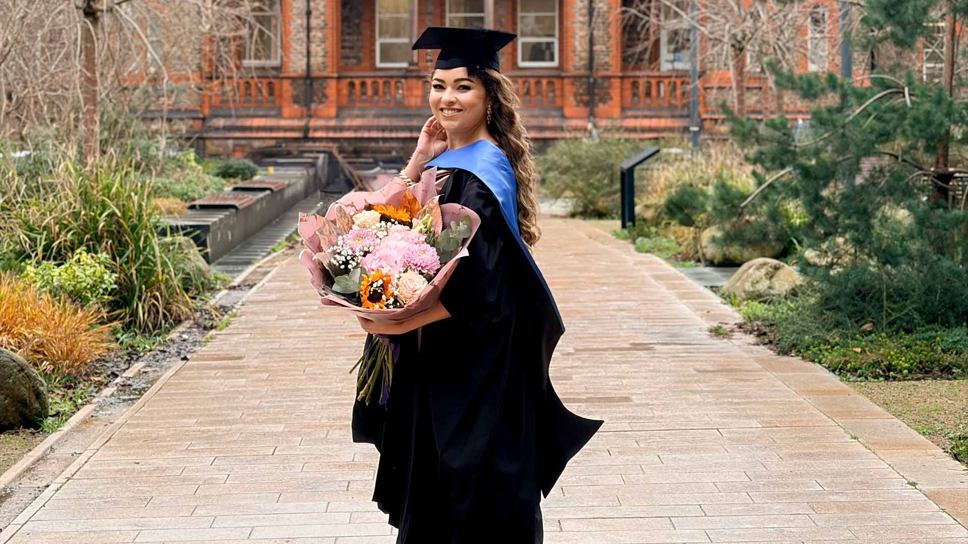 Graduate poses with a bouquet of flowers on campus
