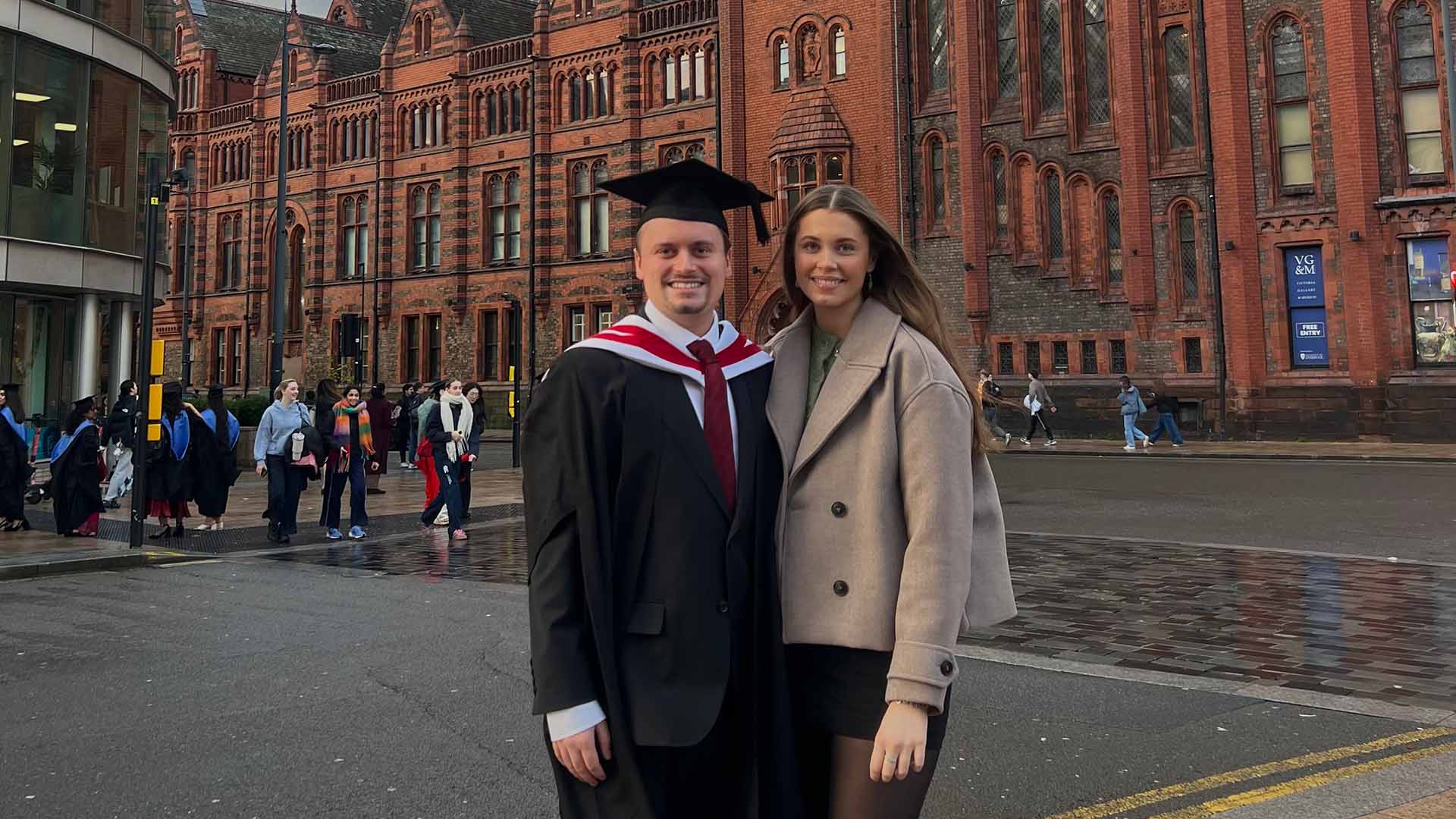 graduate in cap and gown smiles with girlfriend at University Square