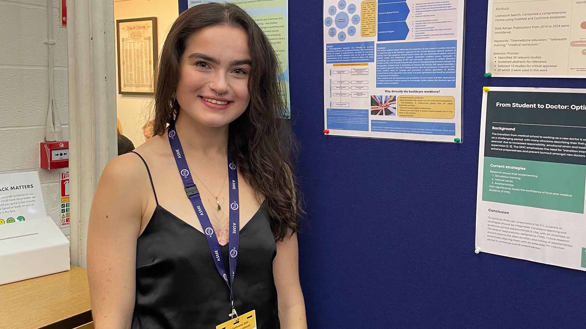 woman with conference lanyard presents in front of a research poster