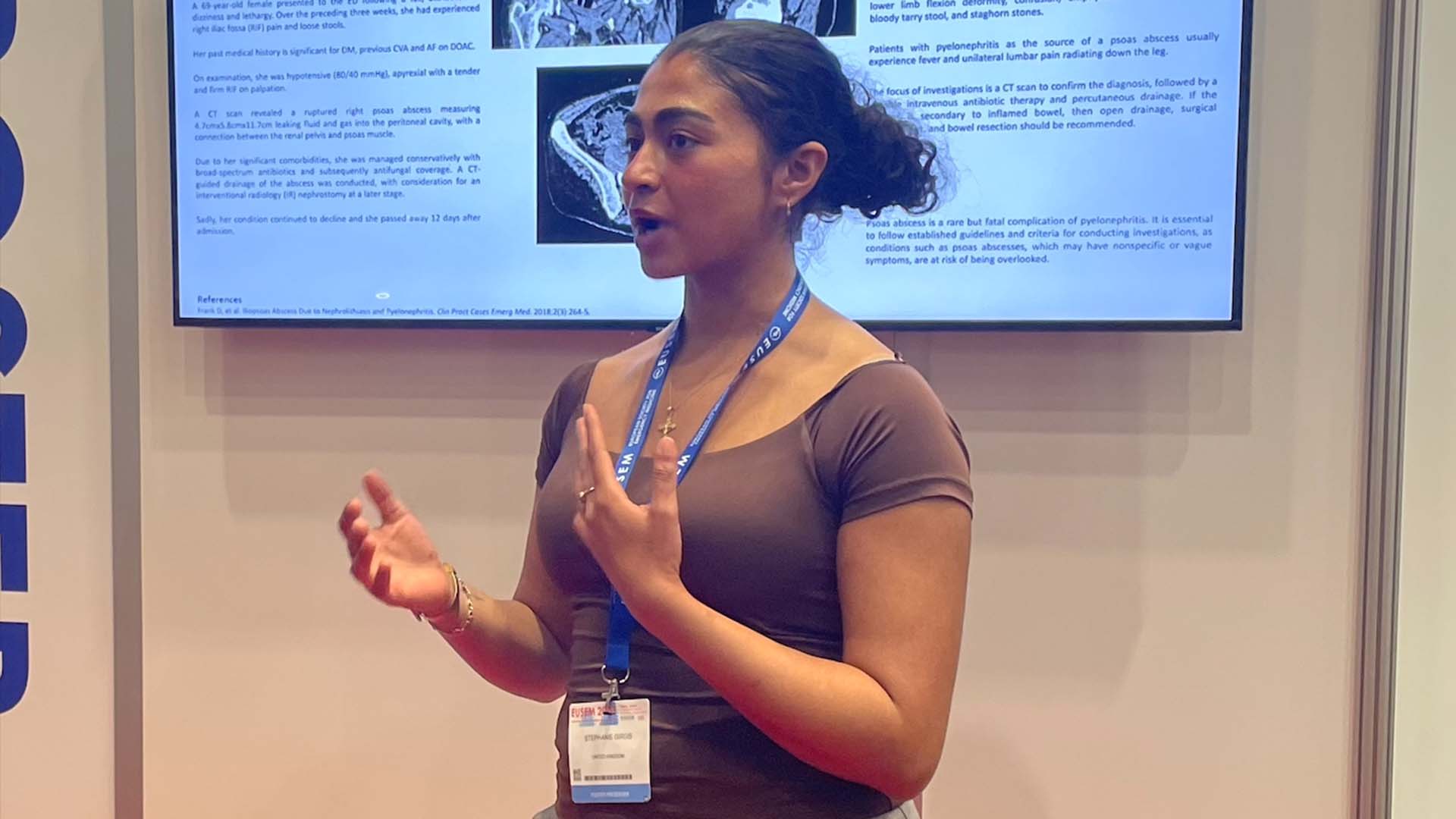 woman with conference lanyard presents in front of a research poster on a digital screen