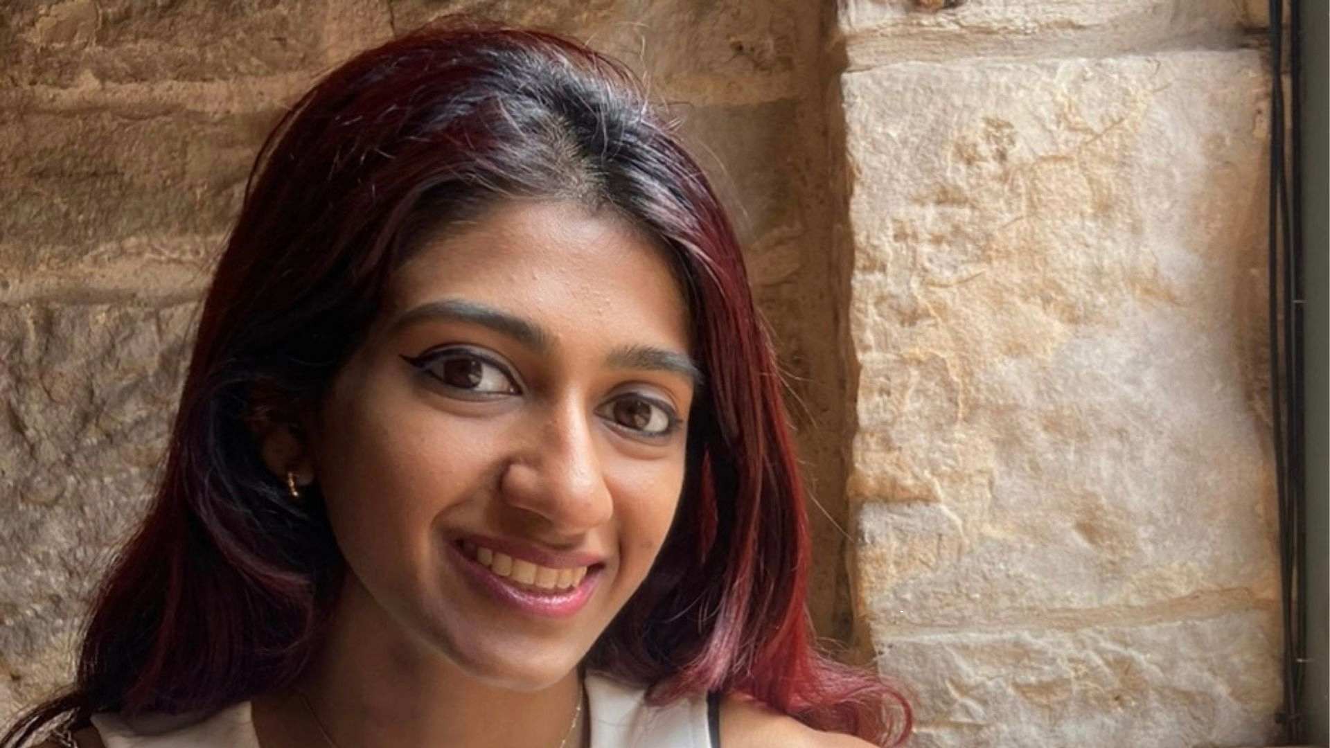 Meera Shankar smiling indoors beside a stone wall