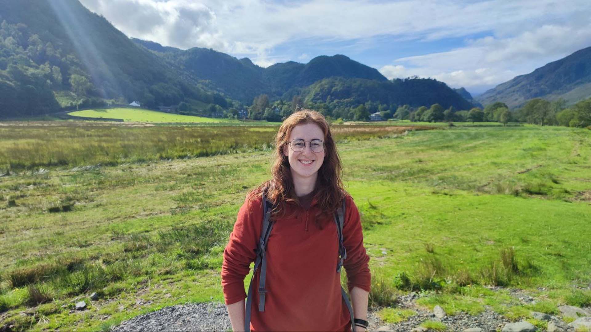 woman in fleece with green fields and mountains in the background