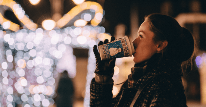 Woman drinking coffee on street with Christmas lights