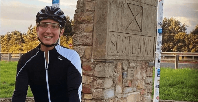 woman student on bike in front of Scotland marker