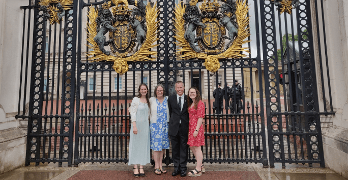 a family in formal wear stands outside the gates of Buckingham Palace