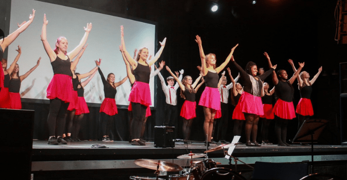 performers in black tops and red skirts dance on stage