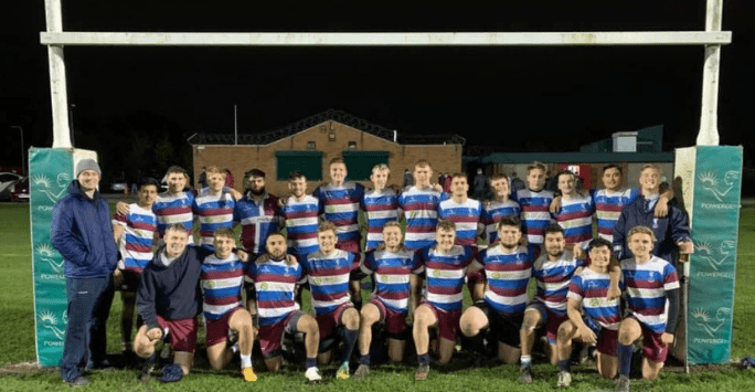 Men's rugby team pose for group shot on rugby pitch