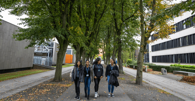 group of students in scrubs walk along a tree lined street on university campus