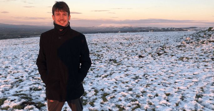 man smiling to camera in snowy field with pink sky