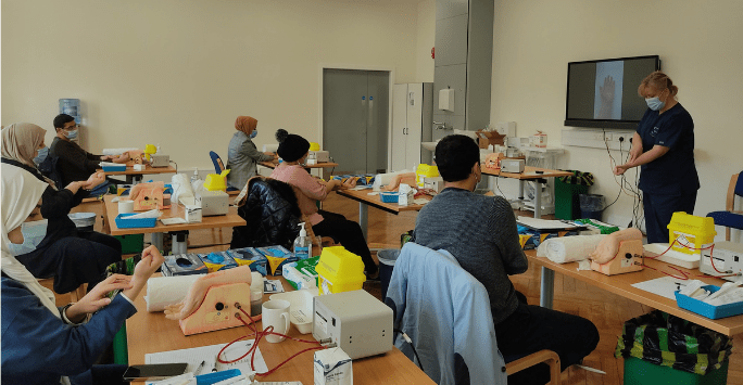 People wearing PPE practice clinical skills in a classroom setting