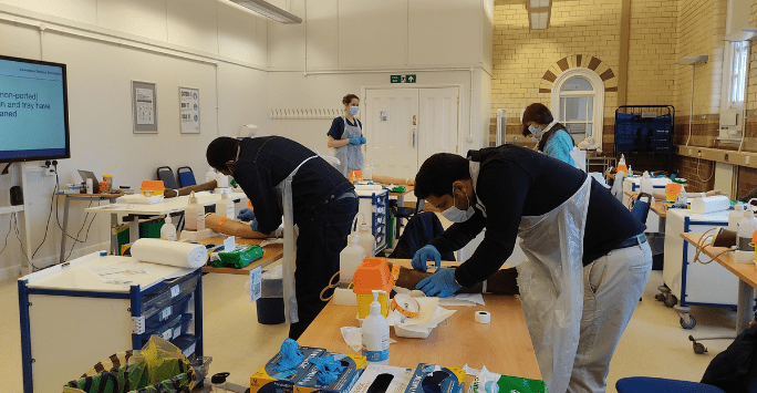 People wearing PPE practice clinical skills in a classroom setting