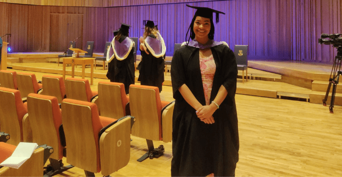 graduate poses in cap and gown in auditorium