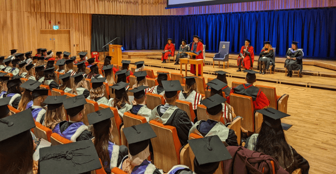 professor addresses graduates in an auditorium