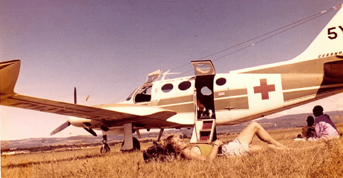 man rests in the grass in front of a light aircraft