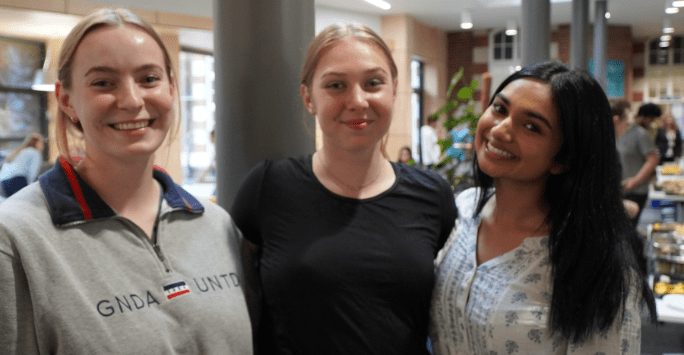three women smile standing in a communal hub area