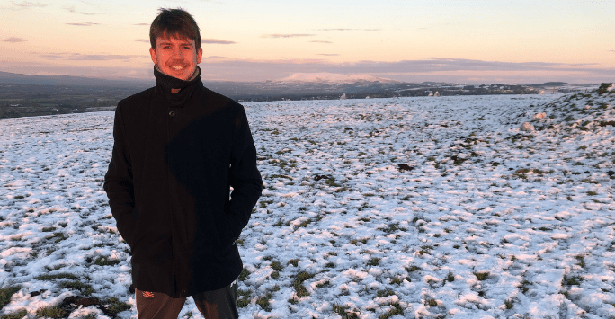man standing in snowy field at sunset