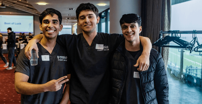 student doctors in scrubs pose with their arms round each other