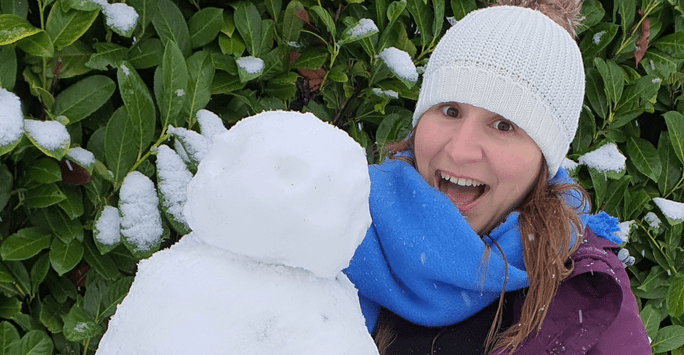 student wearing a hat and scarf poses with snowman