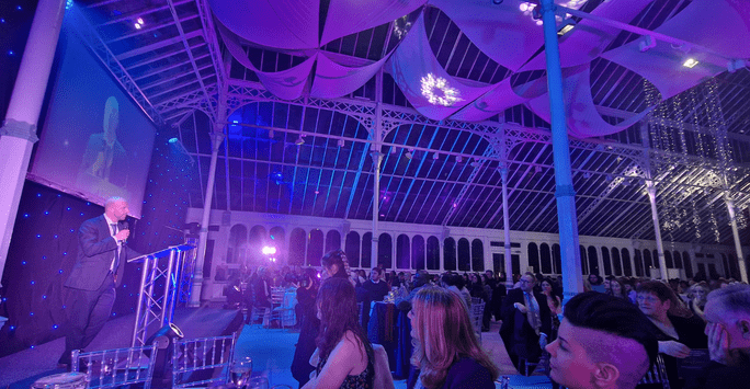man on stage at awards ceremony in glass conservatory