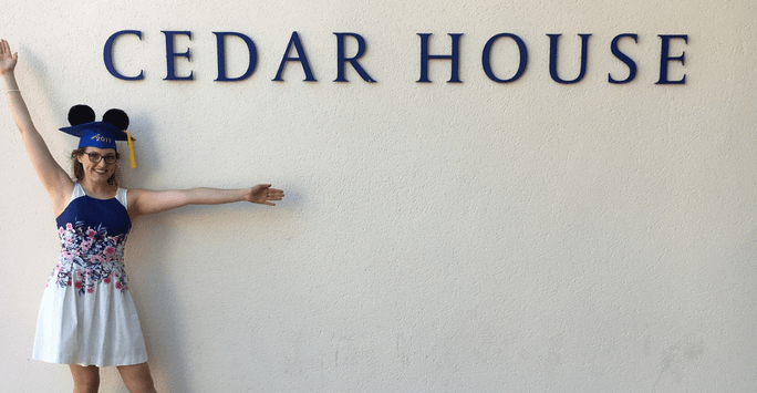 Graduate in Mickey Mouse ears in front of Cedar House sign
