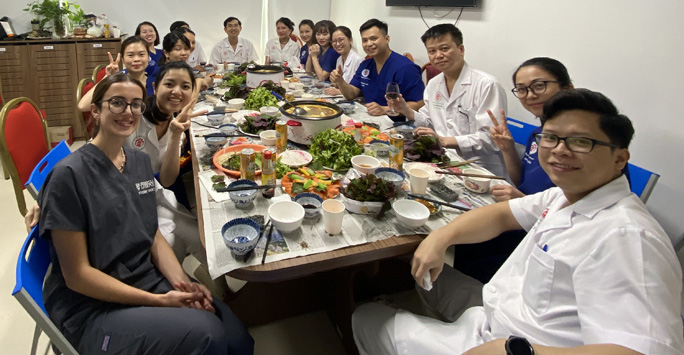 Student Doctor sitting with Vietnamese doctors around large table having a celebratory lunch