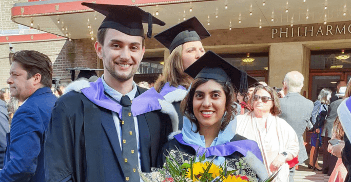 two graduates, one with a bouquet of flowers