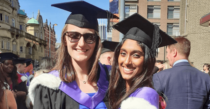two smiling graduates in caps and gowns