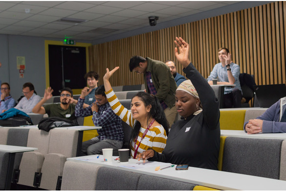 A group of people in a lecture hall raising their hands, indicating participation or questions during a presentation.