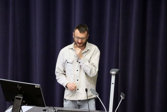 Dr Alexis Makin in a cream jacket and jeans stands in front of blue curtains