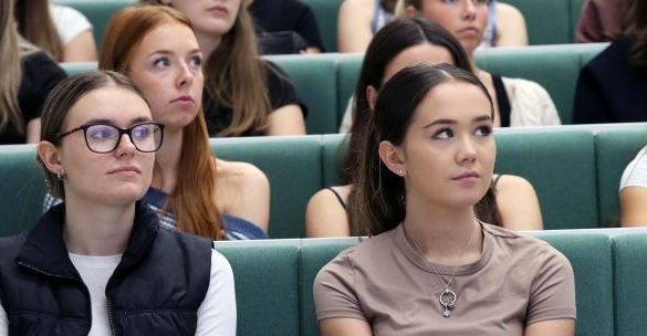 Students sit in rows on green seats