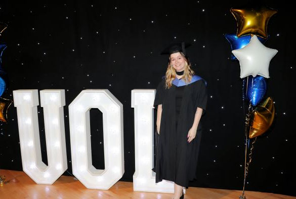 Student in graduation robes by UOL sign