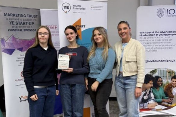 Four students stand in front of a banner holding an award