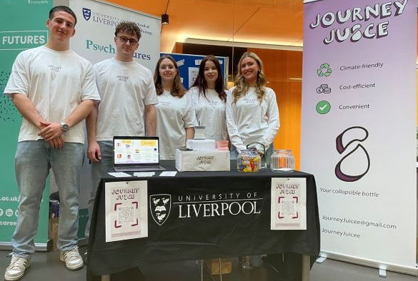 Students in white tops stand in front of display boards