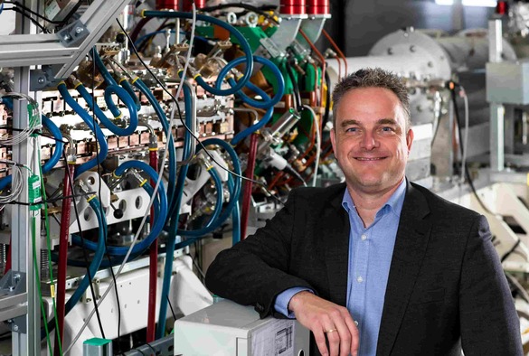 Professor Carsten P Welsch standing next to an industrial machine