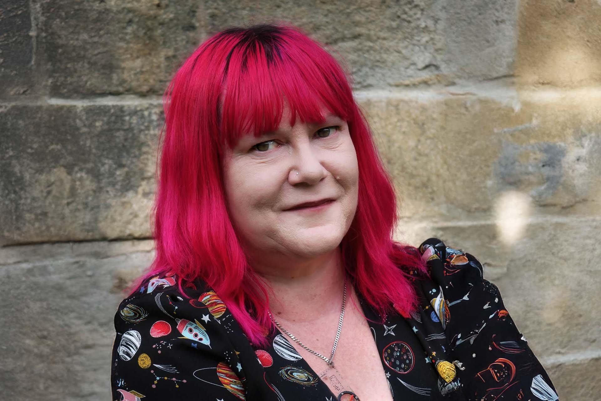Dr Rose headshot, standing in front of a stone wall.