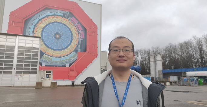 Dr Liu standing smiling near a large mural