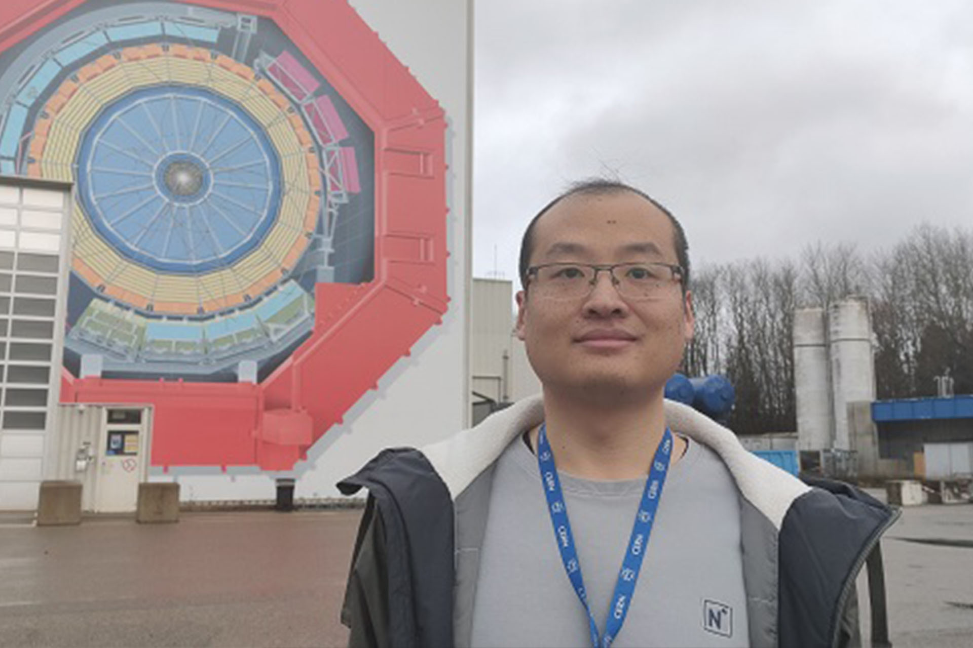 Dr Liu standing smiling near a large mural