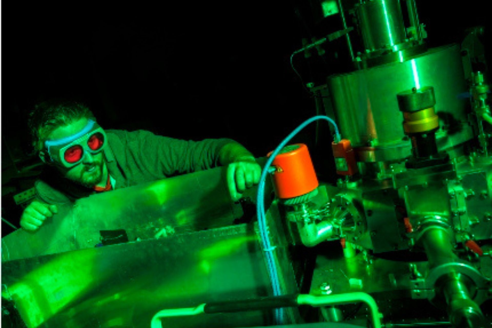 A researcher wearing protective goggles working with machinery bathed in green light