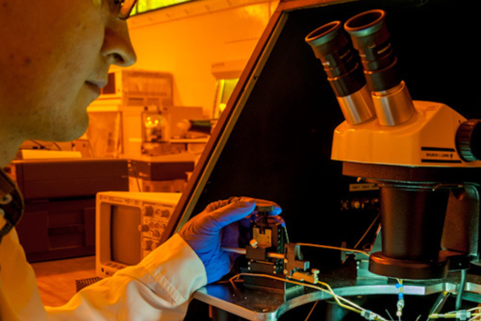 A researcher working with small electronics while looking through a microscope