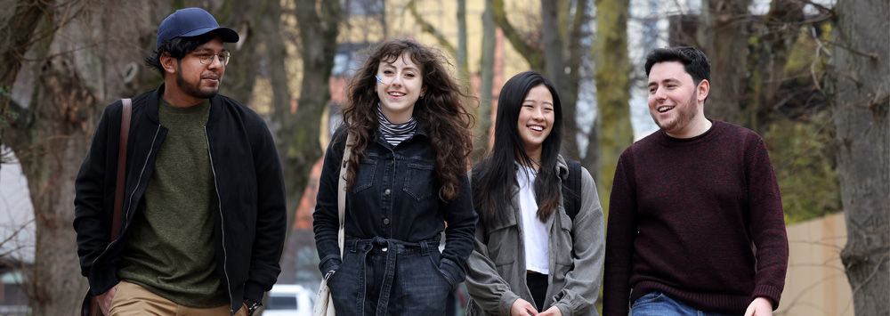 Four students walking through campus together on autumn day.