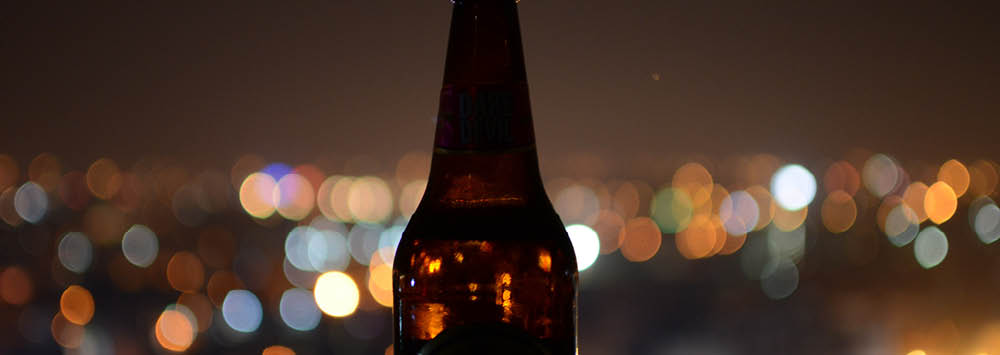 Beer bottle sat on a table with lights in the background.