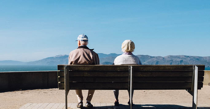 An ageing couple sat on a bench overlooking mountains.