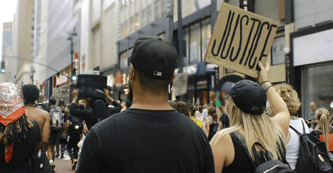 A crowd of people walking through the street holding up a sign that reads 'Justice'.