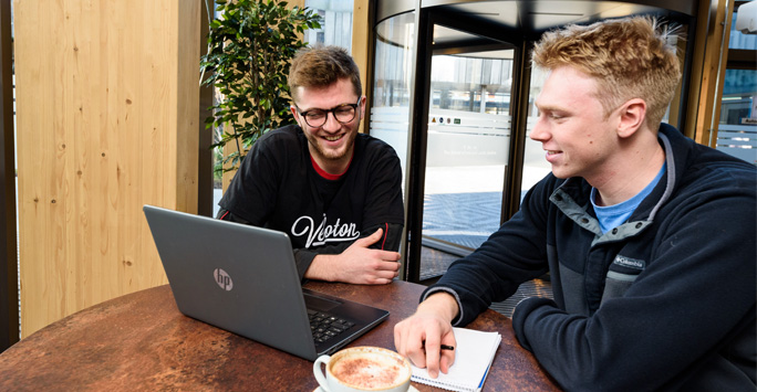 Two students sat a laptop together in the SLSJ Building foyer.