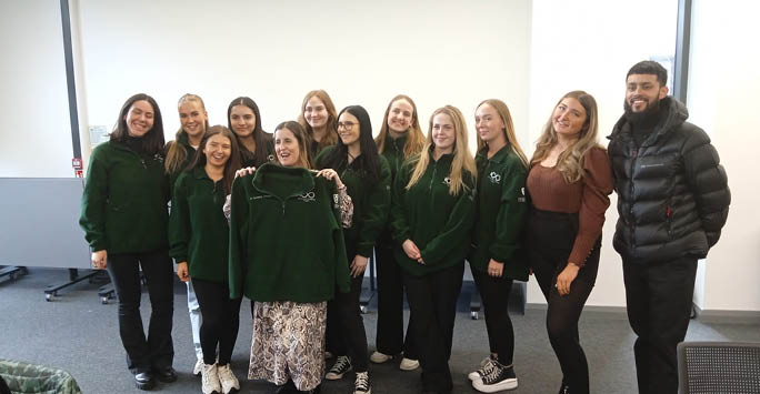 A group of students gathered for a photo holding up branded jackets.