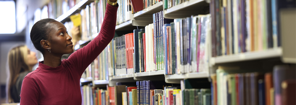 Student reaching for a book from a bookshelf in the Sydney Jones Library